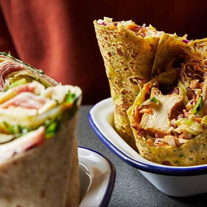 A person picks up a chicken wrap cut in half from a metal plate.