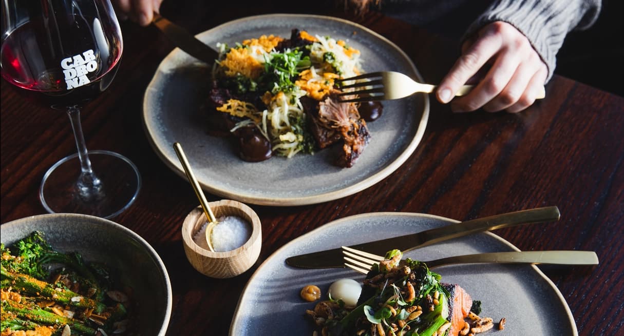 Elegant plated dinner with meat and greens, paired with red wine and gold cutlery at Cardrona.