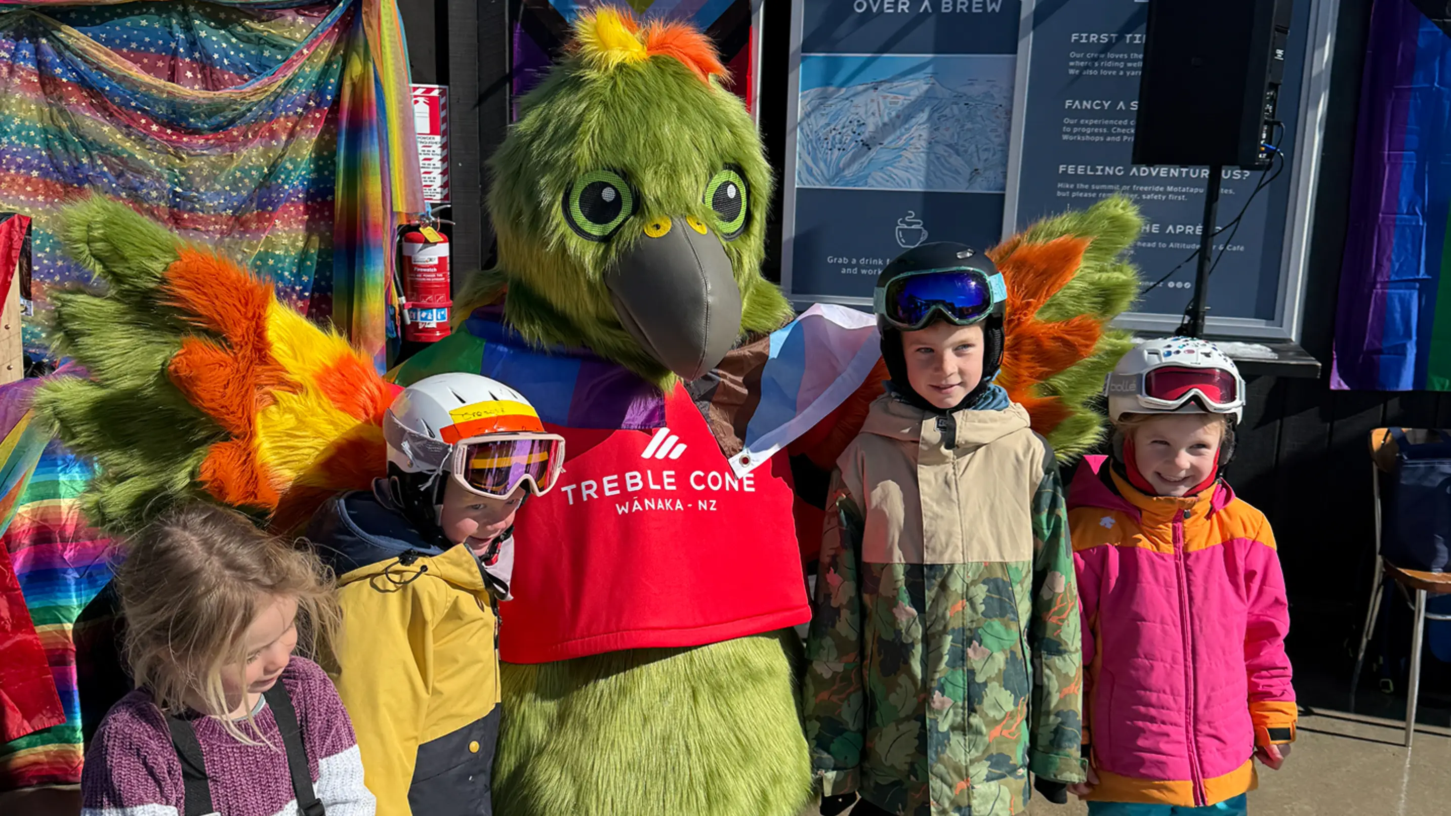 A kea mascot poses for a photo with a group of young kids on a ski field.