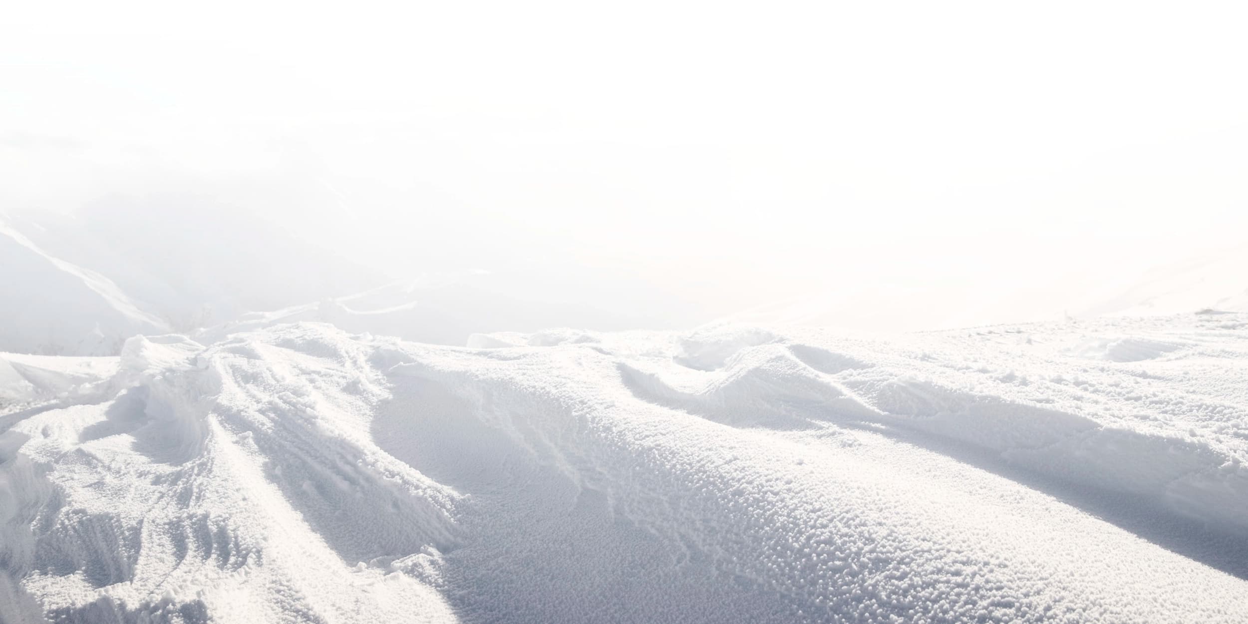 A serene, snow-covered mountain landscape, with soft, undulating slopes bathed in a misty haze.