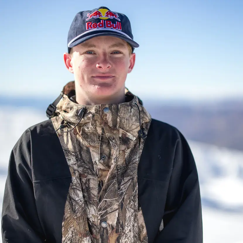 Headshot of New Zealand skier, Luke Harrold standing on a snowy mountain wearing a Red Bull cap and North Face jacket.
