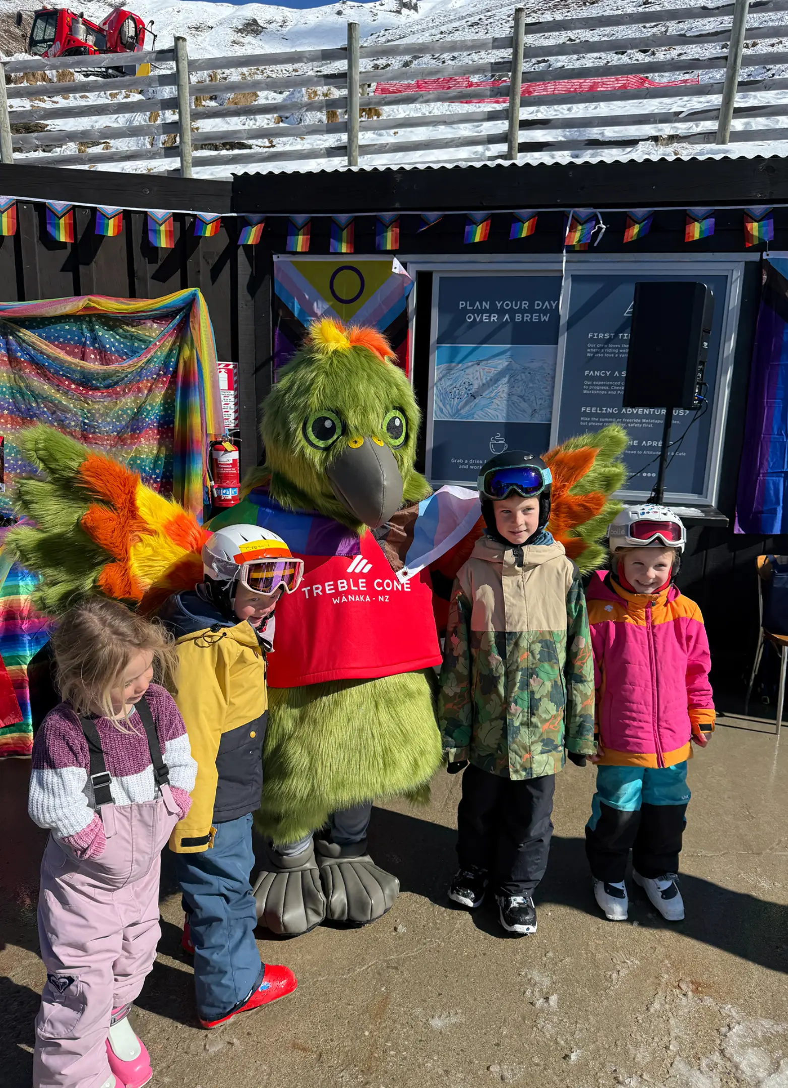 A kea mascot poses for a photo with a group of young kids on a ski field.