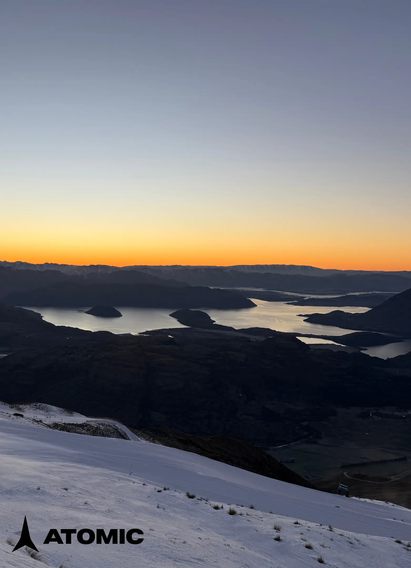View of sunrise over a lake from a snowy mountain with Atomic logo in the corner.