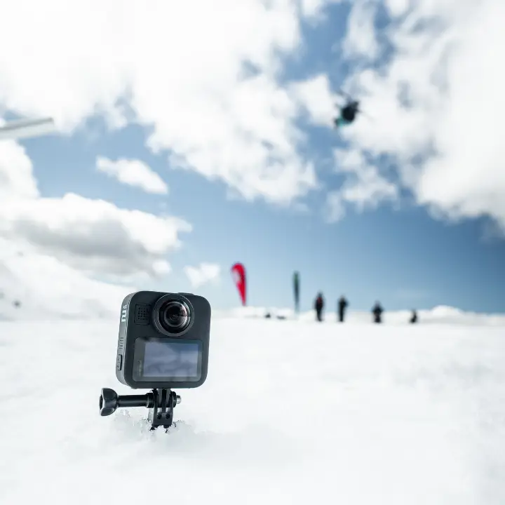 A GoPro standing up in the snow with a skier in the background performing a trick in the terrain park.