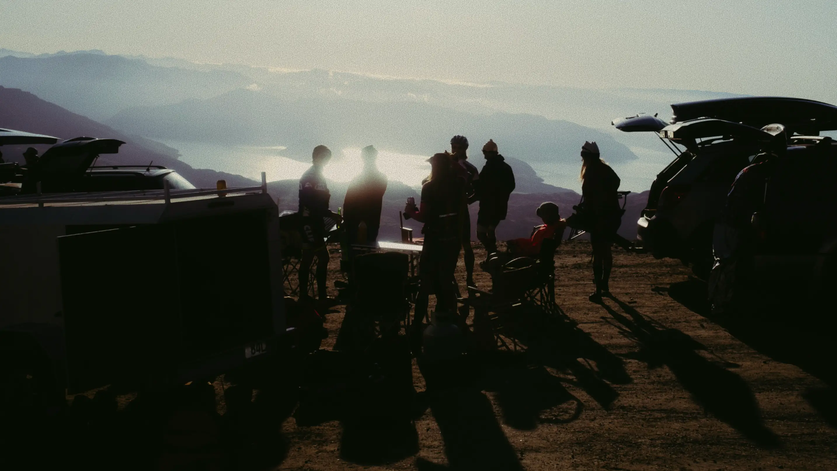 Group of people standing in the car park at the top of ski field at sunrise.