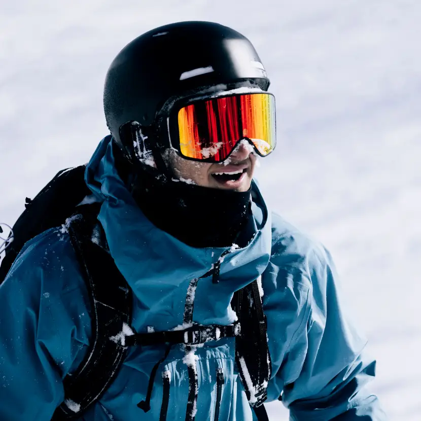 Ben Barclay, NZ skier, grinning on the mountain, helmet and goggles dusted with snow.